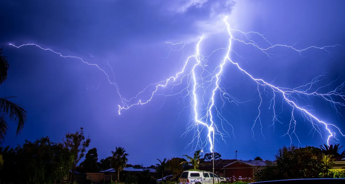 Lightning striking down toward trees and rooftops in a residential neighborhood at night